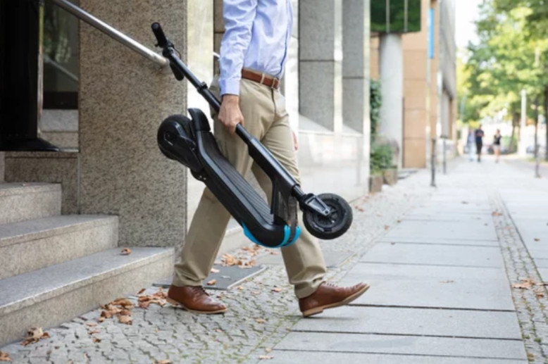 Mit einem E-Scooter bist du jederzeit und überall flexibel unterwegs Mann läuft mit eingeklapptem E-Roller über den Bürgersteig