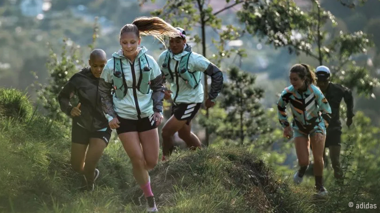 Mit adidas immer sportlich unterwegs Eine Gruppe von Menschen joggt durch die Natur